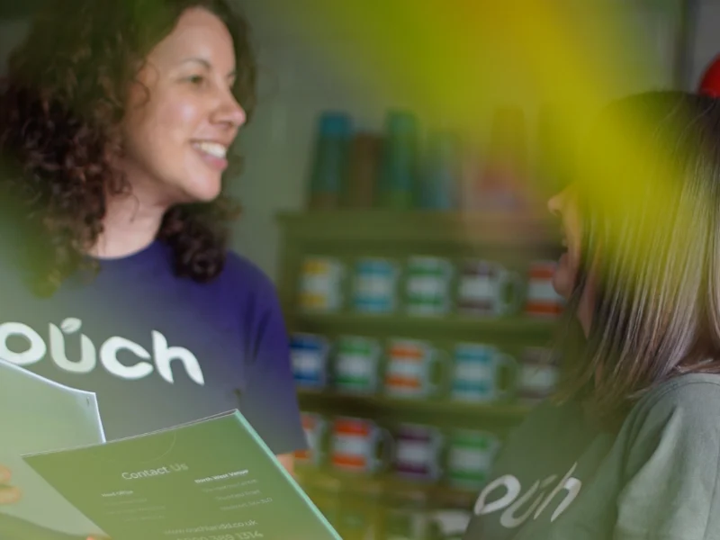 Two Ouch Learning and Development staff in branded T-shirts, one holding a leaflet