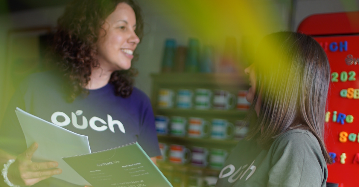 Two Ouch Learning and Development staff in branded T-shirts, one holding a leaflet